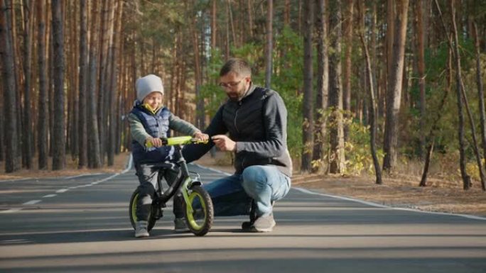 年轻的父亲教小儿子骑平衡自行车