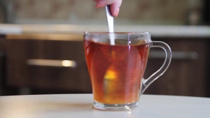 将糖搅拌并溶解在玻璃杯或杯子中的茶中
