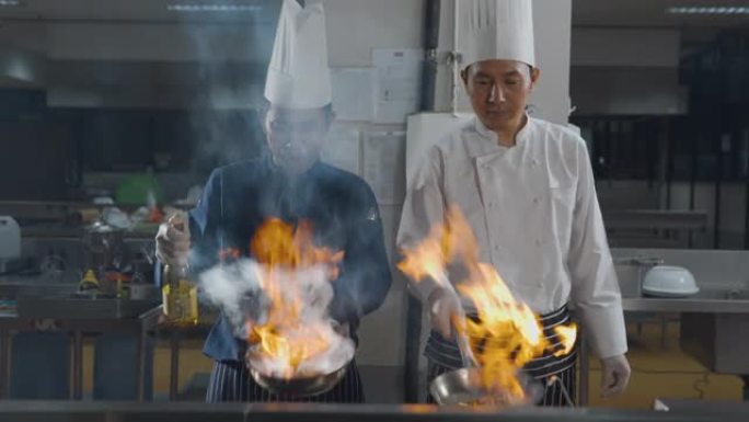 两名厨师在厨房用燃烧的火烹饪食物