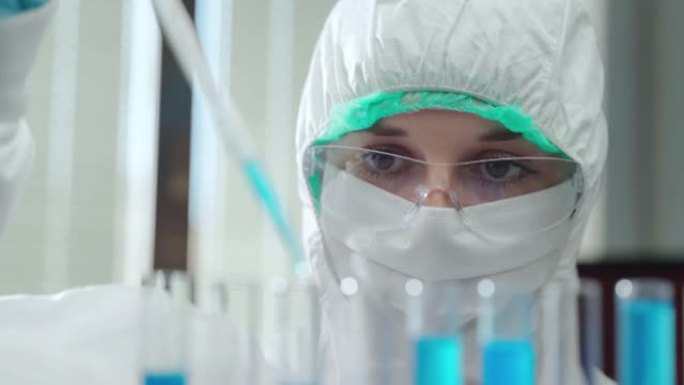 使用无菌测量移液管和滴液在试管中使用防护服和眼镜的女性实验室研究人员的特写镜头。集中化学家在实验室进