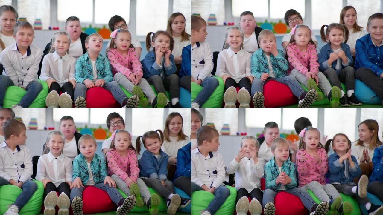 儿童组，快乐健康的孩子和唐氏综合症的孩子一起坐在室内豆袋椅上的相机鼓掌