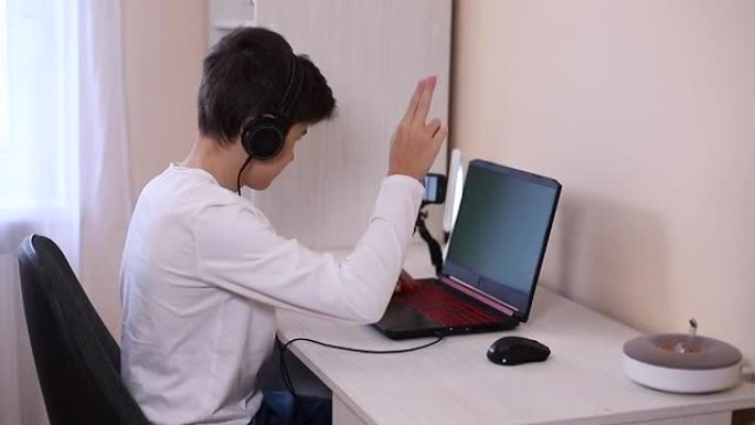 十几岁的男孩在白色房间的电脑上玩游戏。玩家在笔记本电脑上的网络摄像头和三脚架上的手机上捕捉视频，并对