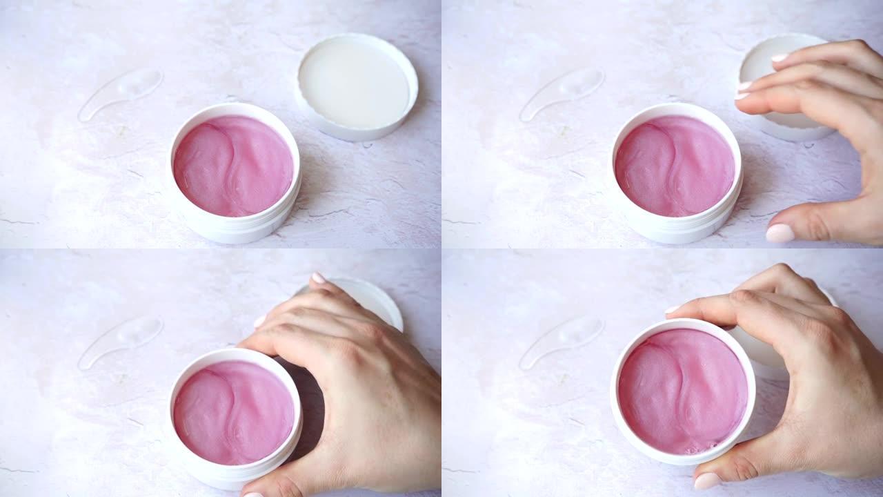 女性手中的水凝胶粉色化妆品眼贴罐。