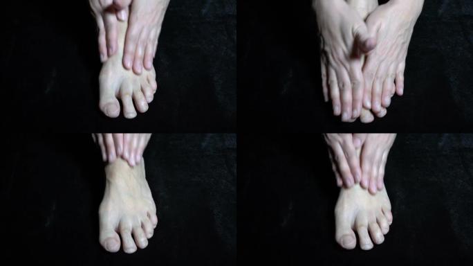 女人的手在黑色背景上摩擦裸露而麻木的脚。特写。顶视图。复制空间。4K。