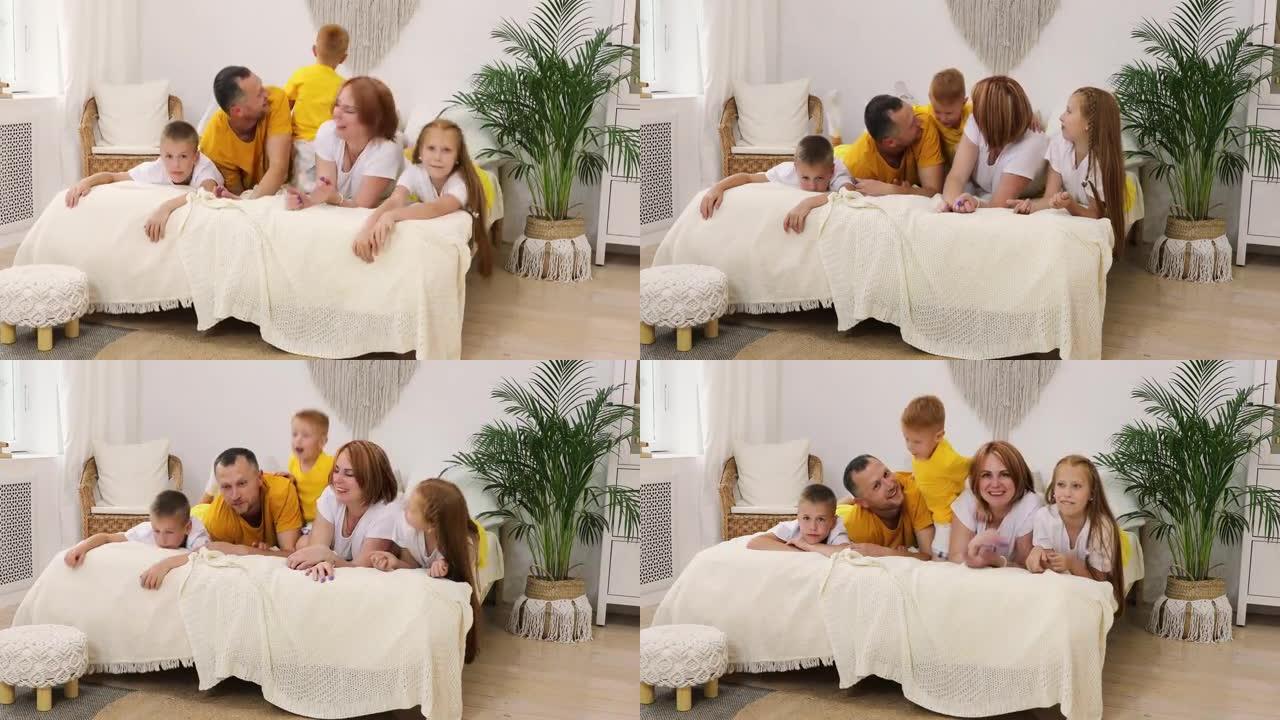 六口之家幸福的大家庭躺在家里的床上玩得开心。一家人挥舞着他们的手