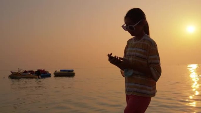 快乐的亚洲女孩站在海里，在自拍后用智能手机看照片，生活方式概念。