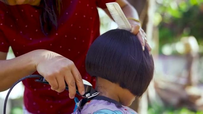 亚洲母亲早上在花园里给女儿剪头发。新型冠状病毒肺炎或电晕病毒大流行期间在家