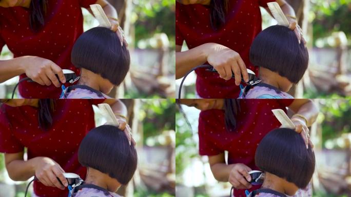 亚洲母亲早上在花园里给女儿剪头发。新型冠状病毒肺炎或电晕病毒大流行期间在家