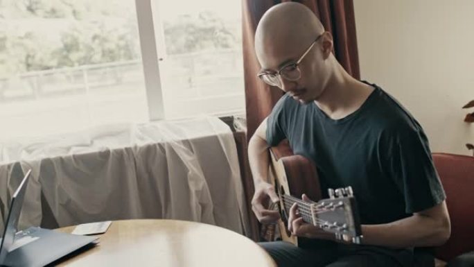 年轻的亚洲人在家里弹吉他