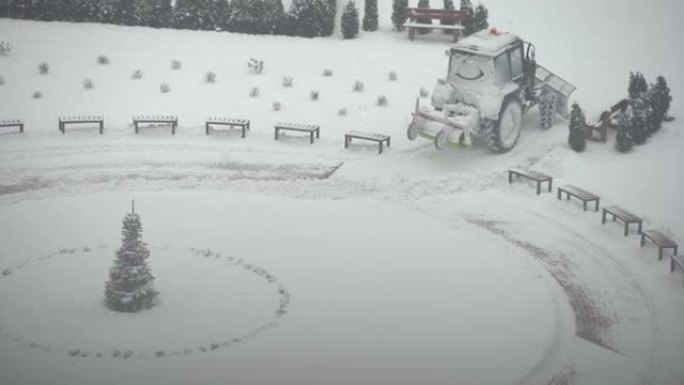 拖拉机-挖掘机清除城市院子里的积雪。公用事业的工作