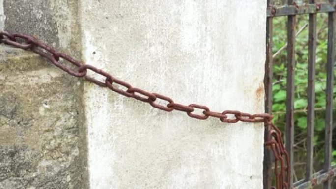 一条生锈的旧链条将铁门绑在混凝土栅栏上