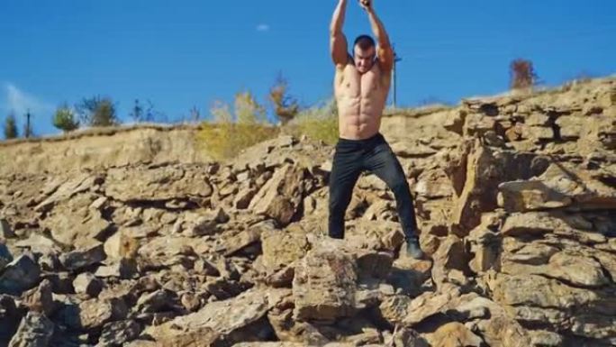 肌肉健美运动员正在山上用钢锤训练。没有衬衫的强壮运动员在户外用金属工具打碎石头。慢动作。