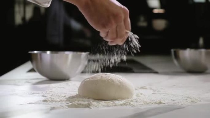 面包店的面包师制作早晨面团，用于烘烤比萨饼，将面粉撒在面团上
