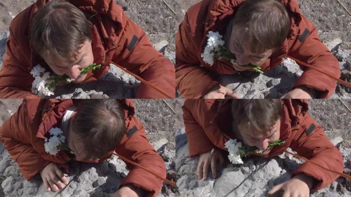 春天特写镜头时，穿着橙色夹克的强壮家伙，牙齿上有白色雏菊花束，用绳子从陡峭的悬崖上爬下来