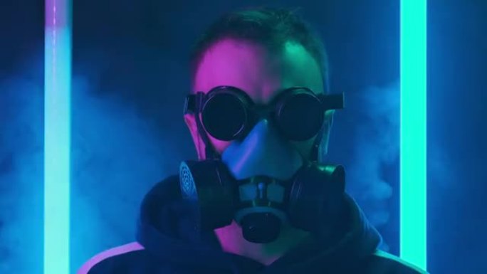 戴着防毒面具的危险男性在闪烁的蓝色霓虹灯和背景烟雾中。