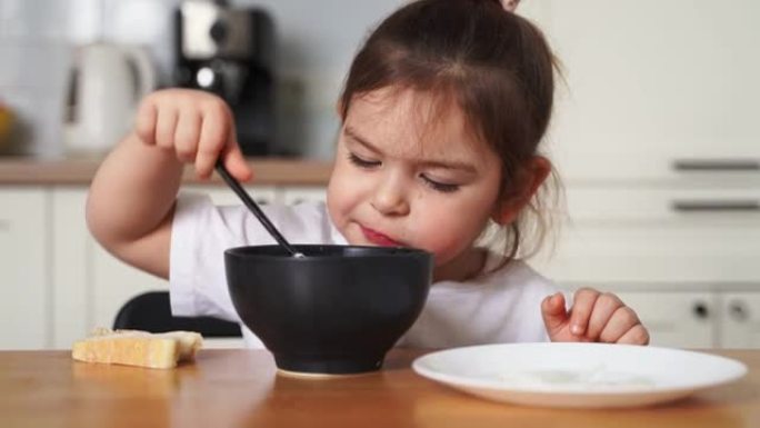 蹒跚学步的女孩在家庭厨房挑食。学习用勺子吃饭。孩子的不良餐桌礼仪