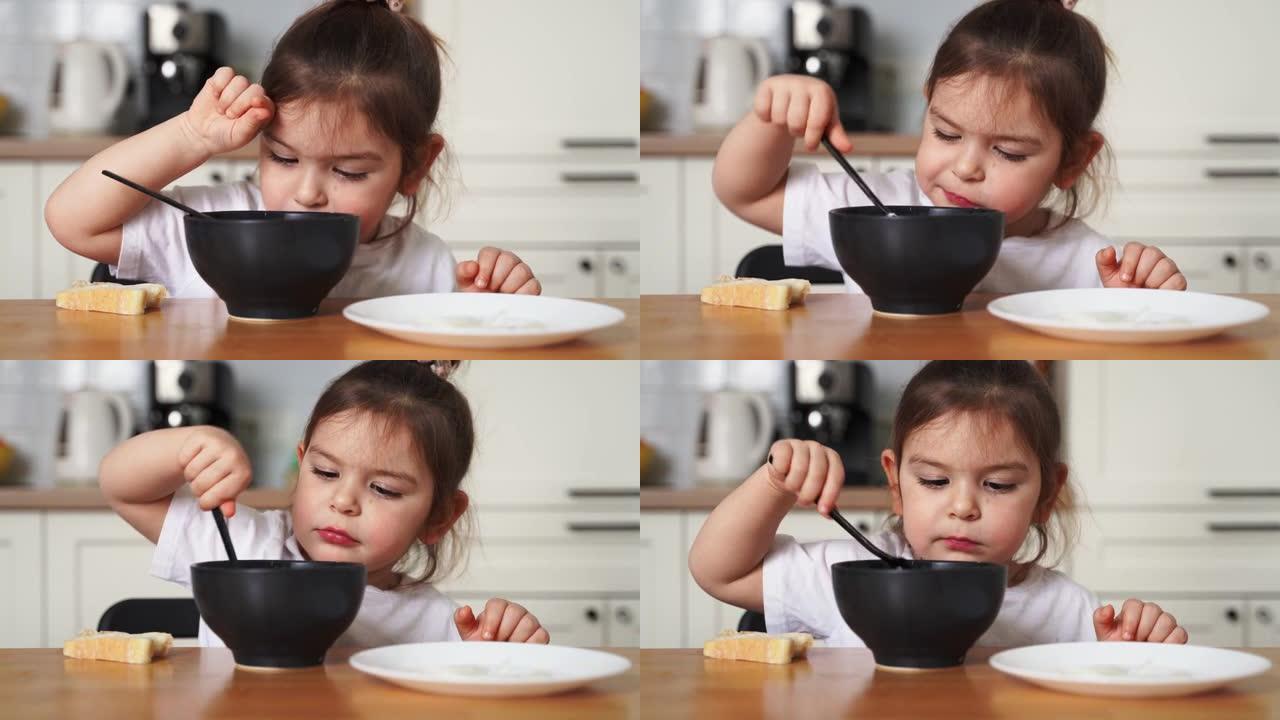 蹒跚学步的女孩在家庭厨房挑食。学习用勺子吃饭。孩子的不良餐桌礼仪