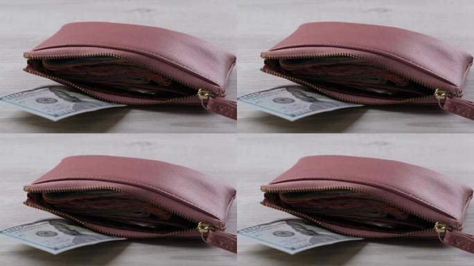 粉红色的钱包，上面有一百美元的钞票和很多钱。财务、费用和收入概念