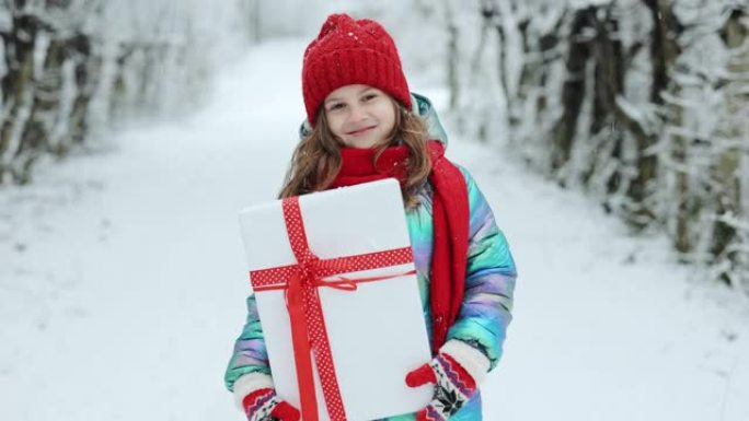 快乐的童女带着圣诞礼物在大自然中冬季散步。享受假期的小女孩。冬季背景上有礼品盒的肖像孩子