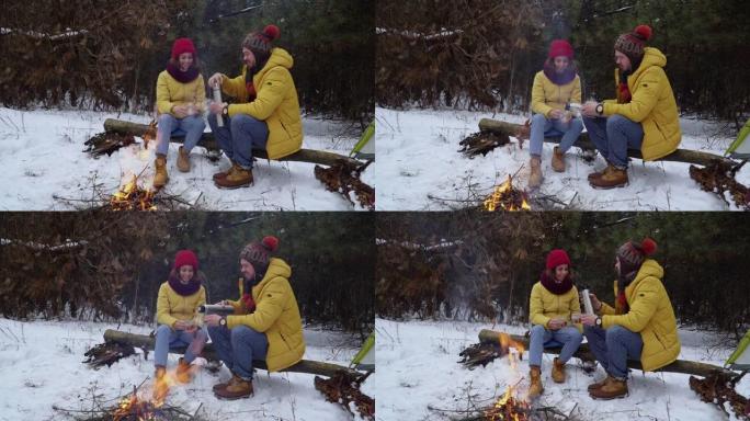 青年男女在冬日森林的炉火旁喝茶