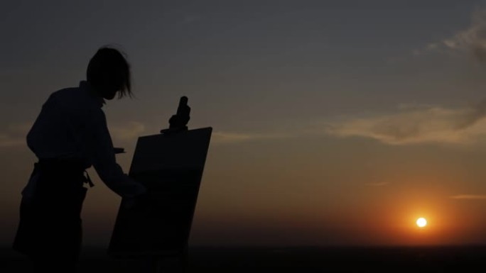 一个在日落时画画的女孩的剪影