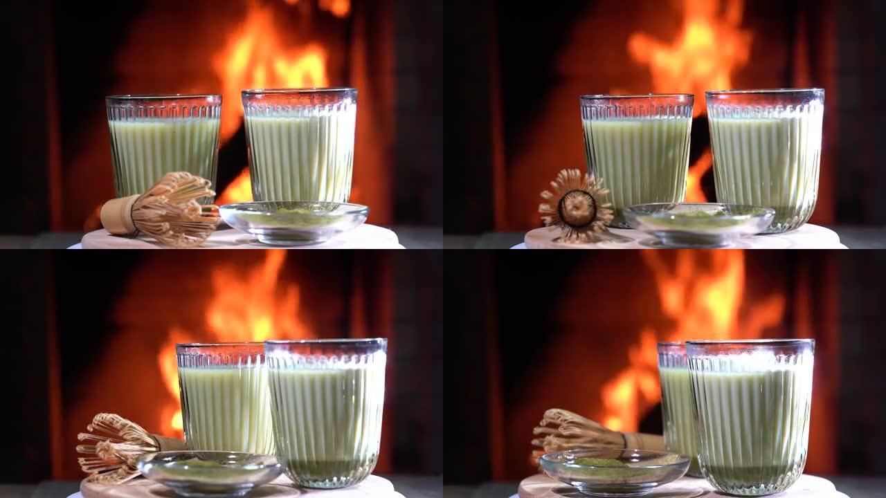 抹茶绿色拿铁茶，抹茶粉和木板上的竹制搅拌器在舒适燃烧的壁炉前旋转。