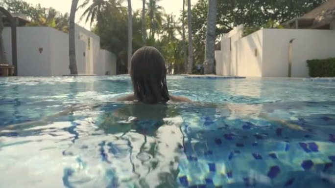 年轻女子走进无限泳池，享受异国情调的暑假奢侈生活方式。