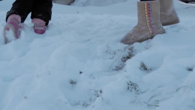 冬季，假期，游戏，家庭概念-慢动作特写婴儿在深雪中行走。孩子们的脚踩在雪道上。寒冷季节的降雪中穿着黑