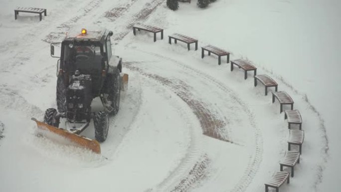 拖拉机-挖掘机清除城市院子里的积雪。公用事业的工作