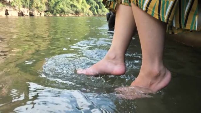 一个穿着休闲服装的长发亚洲女人坐在河里的清水里泡脚