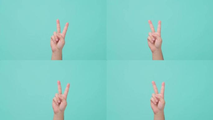 亚洲人类用两根手指举起手的特写镜头，食指和中指举起。该男子在背景的孤立蓝屏中显示v符号胜利手势。