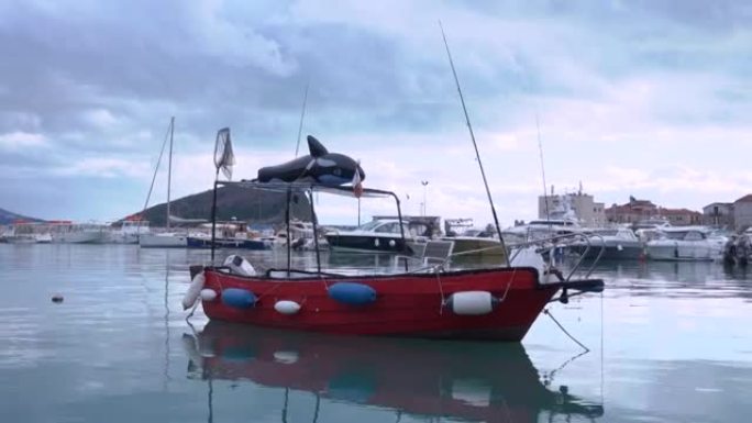 空的红色捕鱼摩托艇，屋顶帐篷上有充气假虎鲸，停泊在城市港口，在平静的夜晚，多云的天空下。