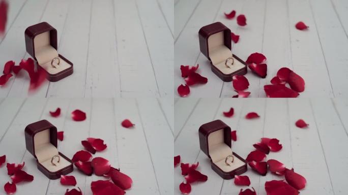 盒子里的戒指放在白色的木头桌子上，玫瑰花瓣落下