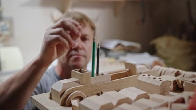 工匠在木工工作室建造木制玩具。熟练的中年木匠在车间组装玩具车时，将铅笔放入木制细节的钻孔中