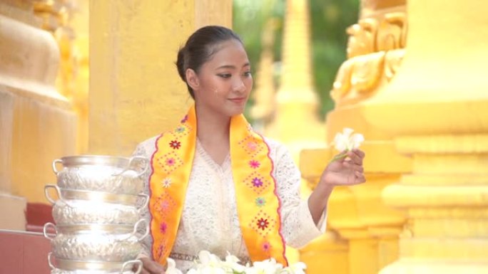 缅甸妇女在寺庙手持鲜花。穿着缅甸传统服装的东南亚年轻女孩参观了一座佛教寺庙。