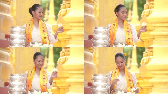 缅甸妇女在寺庙手持鲜花。穿着缅甸传统服装的东南亚年轻女孩参观了一座佛教寺庙。