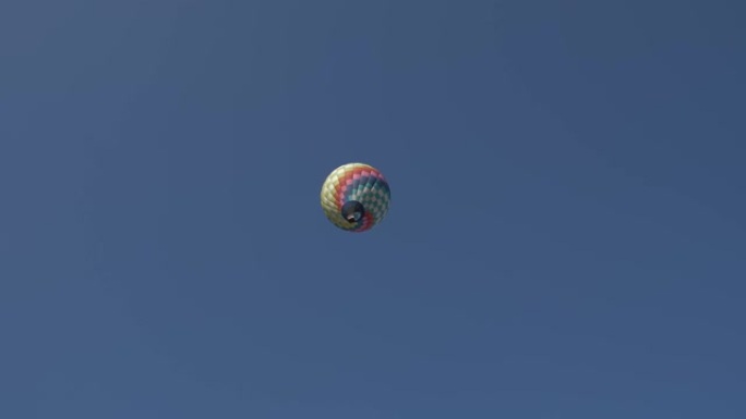 一个带有篮子的彩色热气球在蓝天上飞翔。从地面看。
