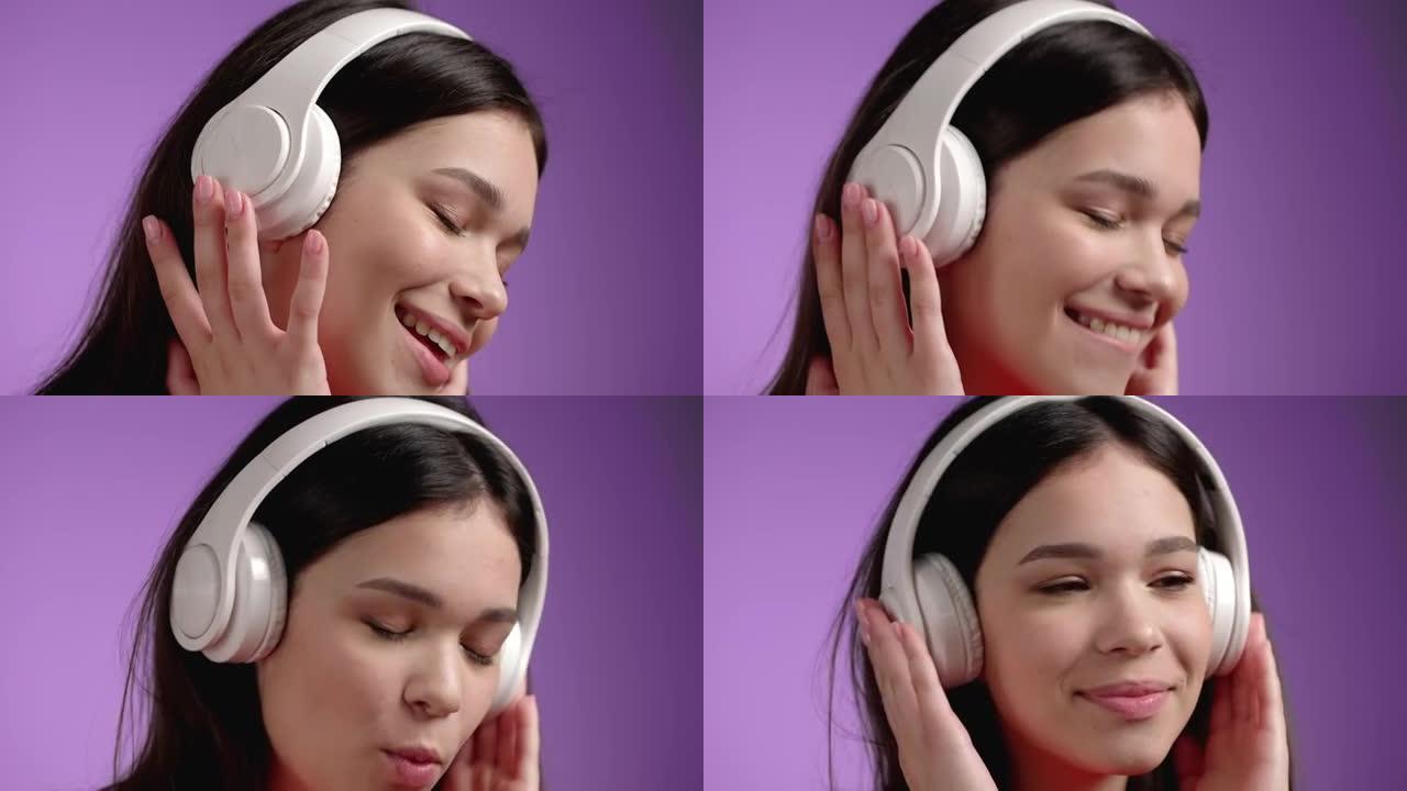 年轻女孩听音乐的特写脸，在紫罗兰色背景下戴着耳机积极跳舞。女人唱歌唱歌。音乐、舞蹈、无线电概念、慢动
