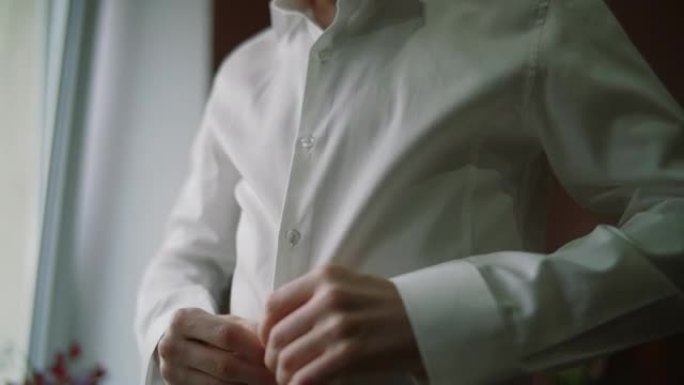 男人在家里打扮和扣上衬衫纽扣的特写镜头。男人扣衬衫。人、生意、时尚