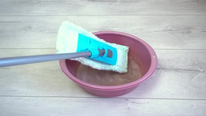 将蓝色拖把放在一碗水中，以便稍后开始清洁磨损地板