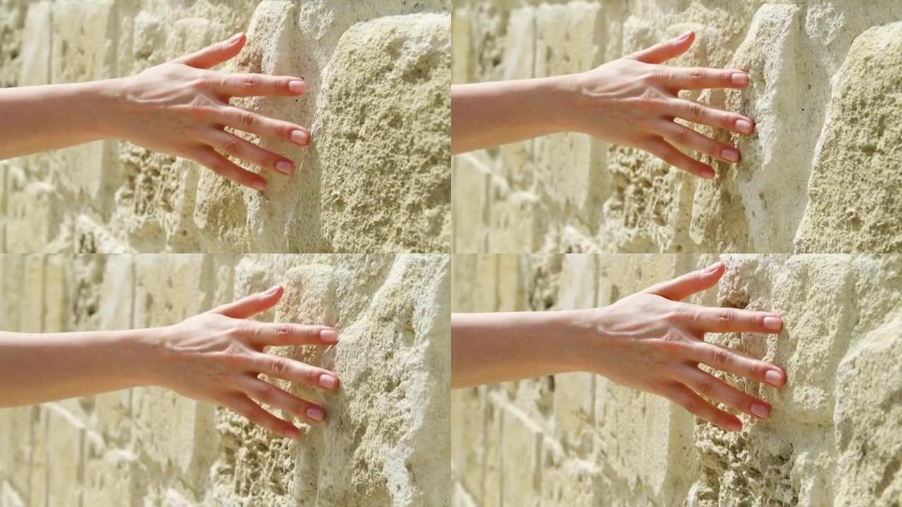 女人在慢动作中滑手靠在旧石墙上。女性手触摸岩石粗糙表面