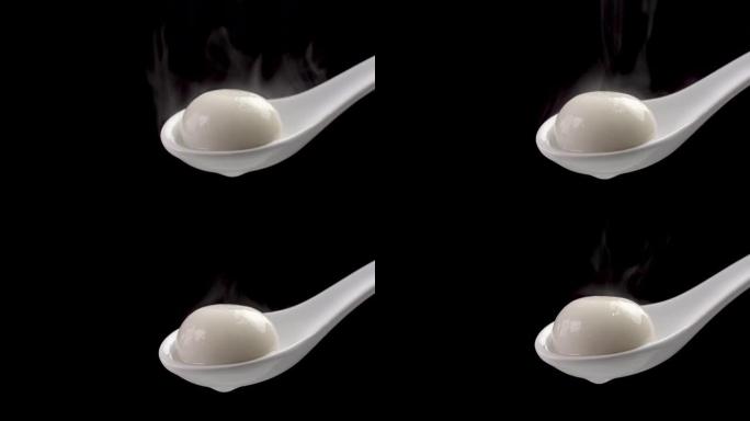 汤圆饭团用热蒸汽在黑色背景上的白色勺子里。