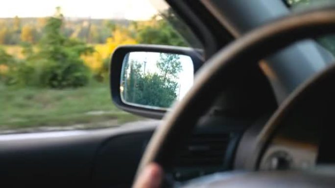 无法识别的驾驶员操纵车辆并穿越乡村高速公路。背景模糊农村环境的汽车后视镜视图。平静的夏季公路旅行。慢