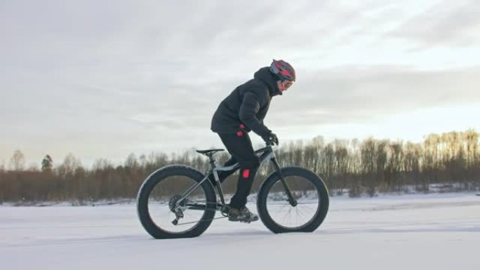 专业极限运动员骑自行车的人在户外骑胖自行车。骑自行车的人在冬天的冰雪上骑行。男人确实在戴着头盔和眼镜