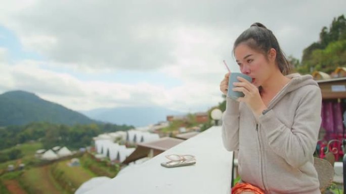 蛤蜊和平年轻迷人的亚洲女人手握热咖啡饮料坐放松看美丽的山景山顶咖啡馆背景旅游概念