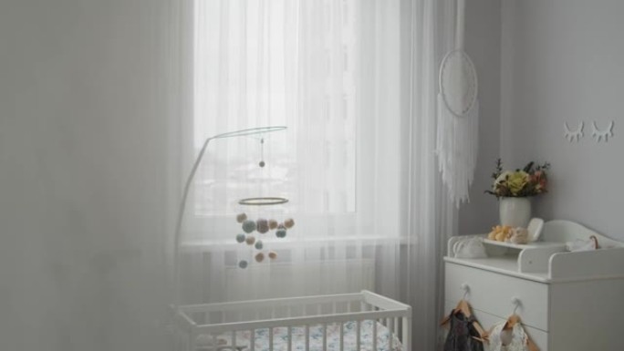 时尚明亮的现代婴儿房内部: 婴儿床、悬挂式手机、更衣桌