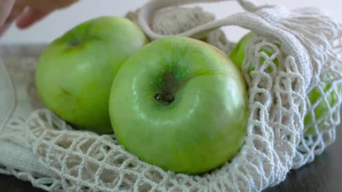 四个大青苹果堆放在一个开放的白色食物篮中。他们拿起网柄，拿起苹果。健康饮食。水果