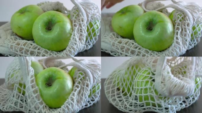 四个大青苹果堆放在一个开放的白色食物篮中。他们拿起网柄，拿起苹果。健康饮食。水果