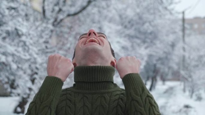 兴奋男子的肖像在冬天下雪的背景上显示是手势。快乐的彩票赢家庆祝成功，对镜头感到惊讶，站在冬季公园的户