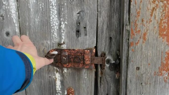 男性的手关上了一扇木门。旧生锈的锁，螺栓